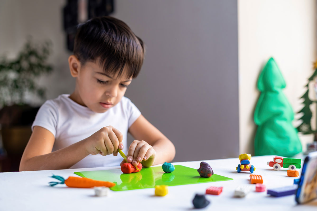 small-caucasian-boy-playing-with-colored-plasticine-making-figures-white-table-happy-child-idea